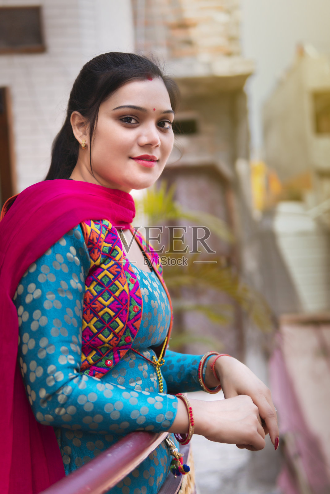 美丽的印度年轻女子站在阳台上，呼吸着新鲜空气，看着镜头。照片摄影图片