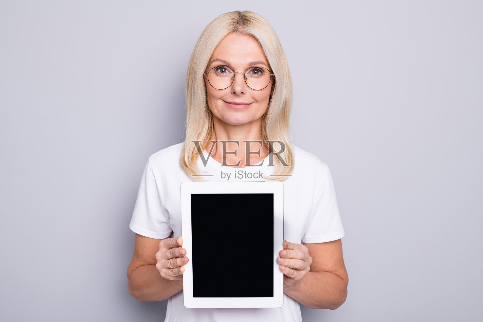 金发乐观的老太太的肖像显示平板戴眼镜白布孤立在灰色背景照片摄影图片