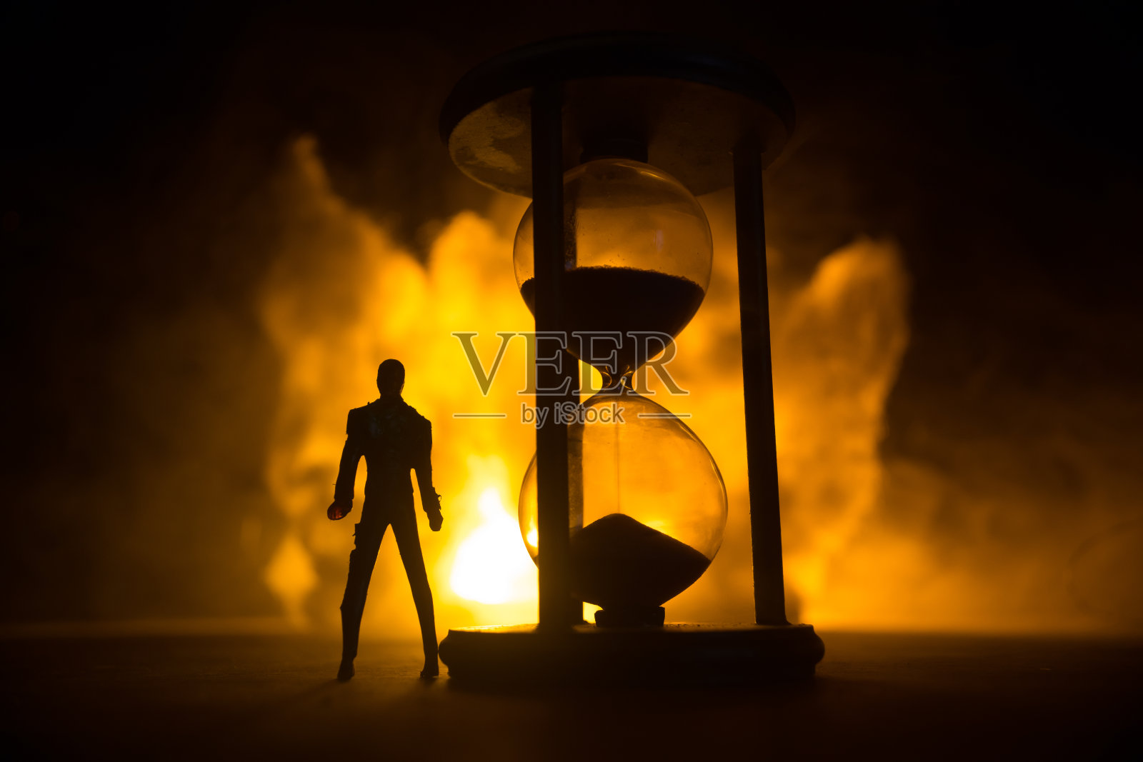 时间的概念。沙漏钟的剪影和带有箭头和烟雾的老式木钟，在深色的背景上配上热的黄橙色红蓝色冷背光，或者是带有复制空间的时间符号照片摄影图片