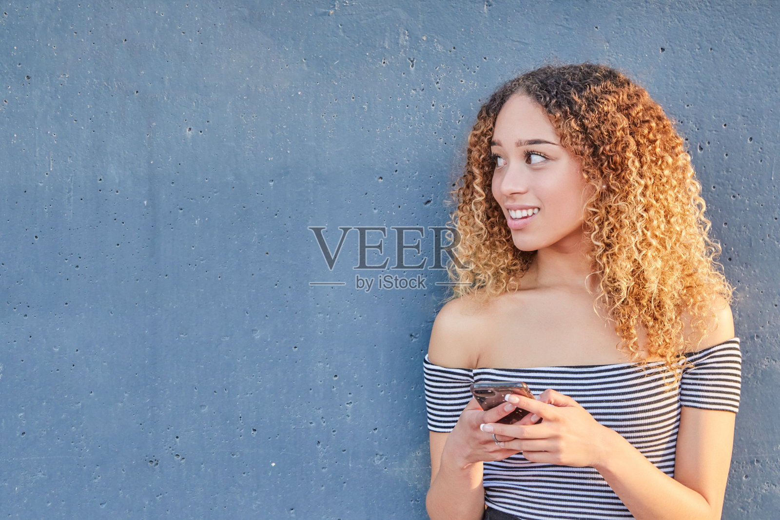 微笑的拉丁裔少女拿着智能手机在家里使用移动应用程序技术。快乐的西班牙小女孩发短信，查看社交媒体应用。照片摄影图片