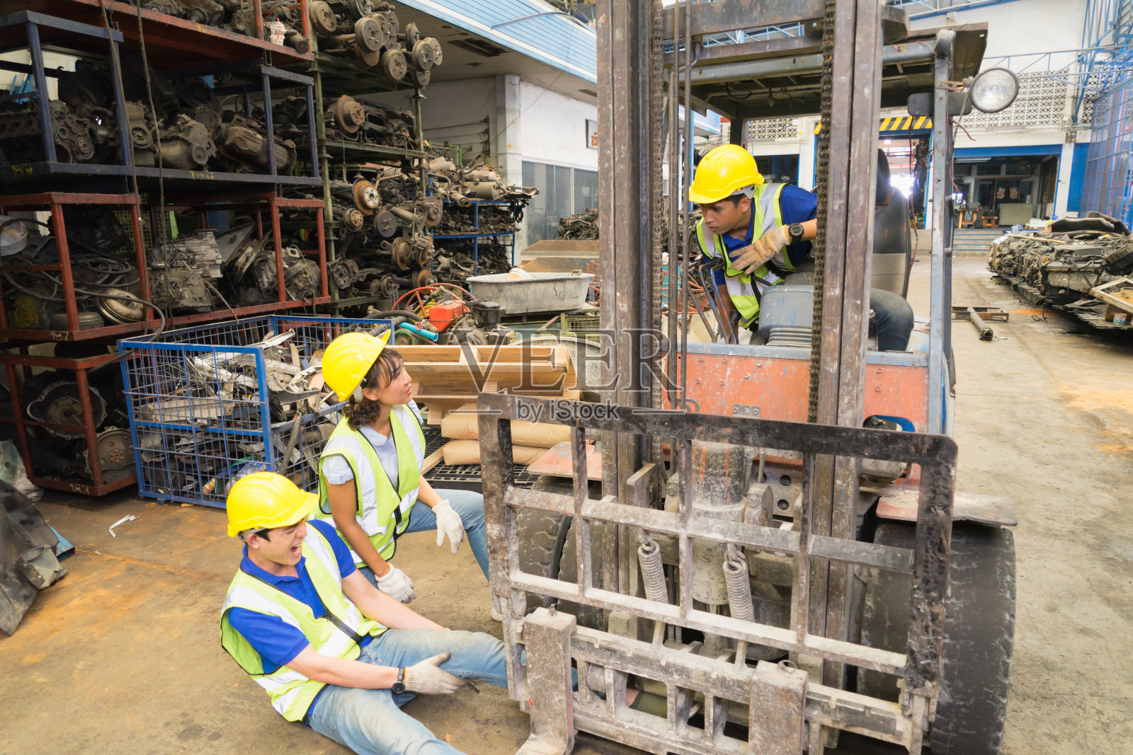 工人大范围事故，叉车压过工程师腿。亚洲工程师工人男子痛苦地被铲车压碎，而工程师妇女在工厂仓库与男子交谈照片摄影图片