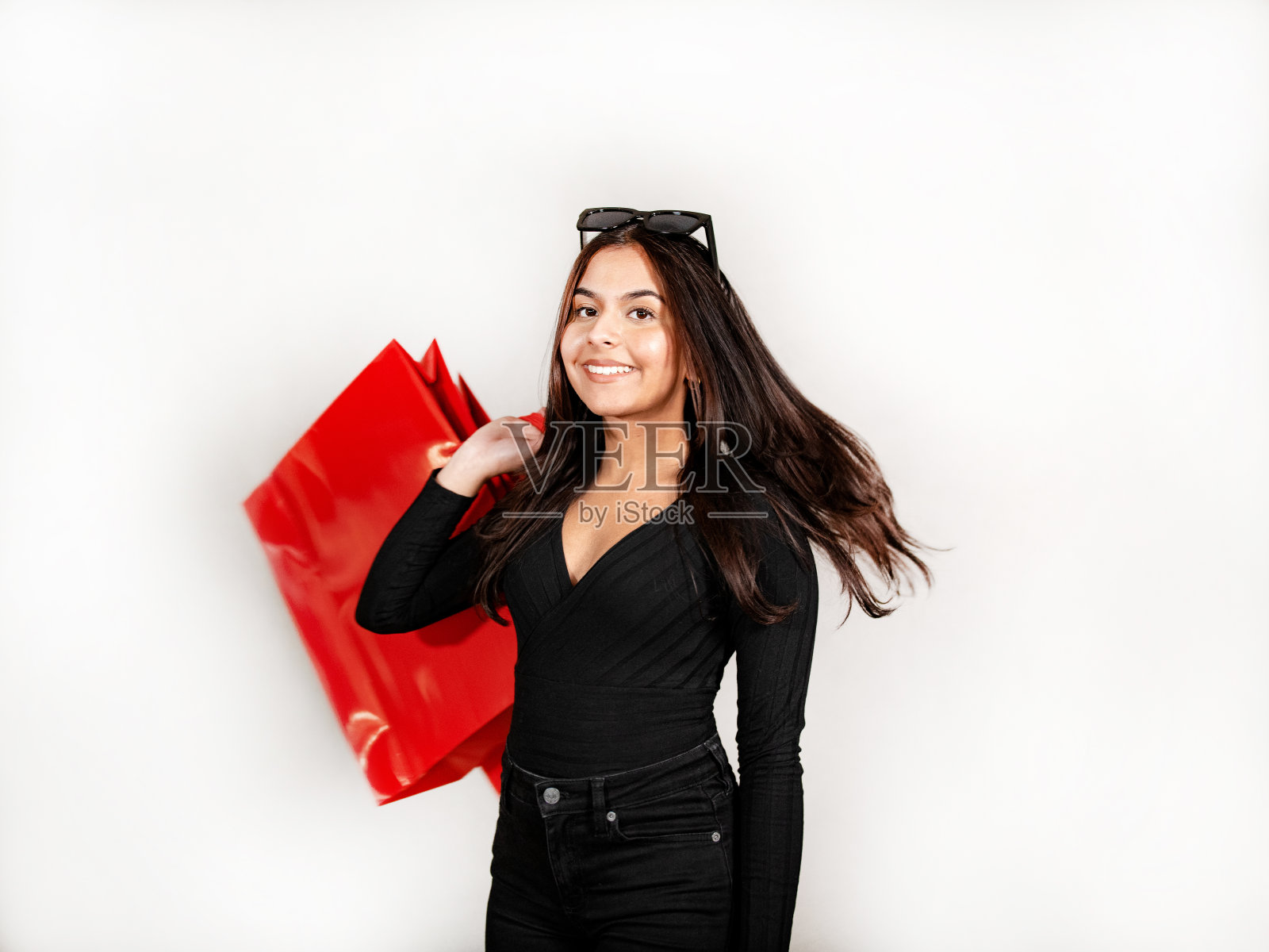 棕色头发，黑色牛仔裤和运动衫的女人拿着一个红色的购物袋。照片摄影图片