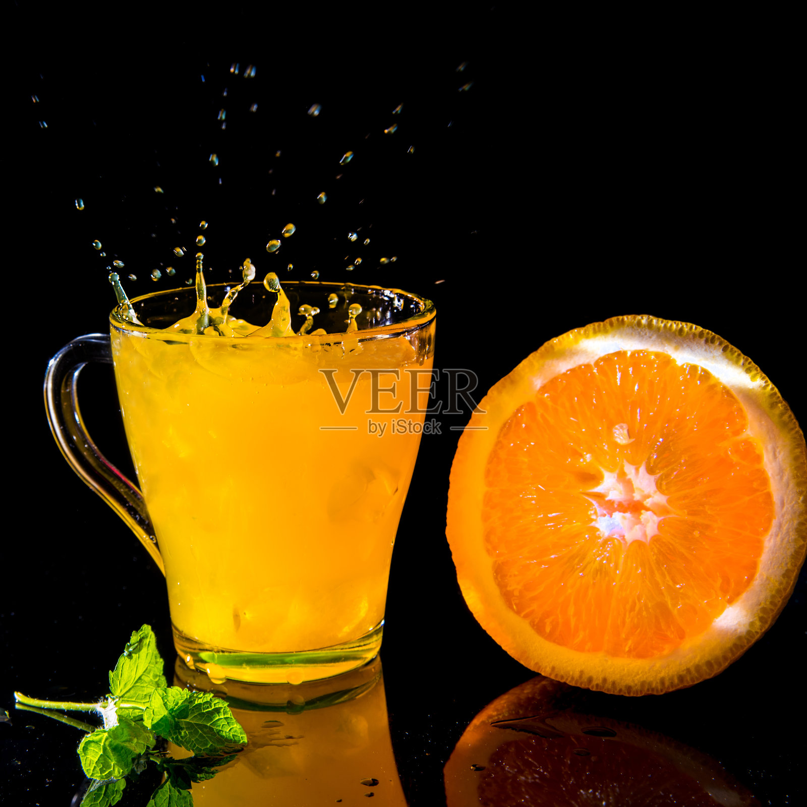 在玻璃杯中加入橙汁和薄荷，在黑色的背景上加半个橙子，健康的生活方式概念，复制空间，悬浮照片摄影图片