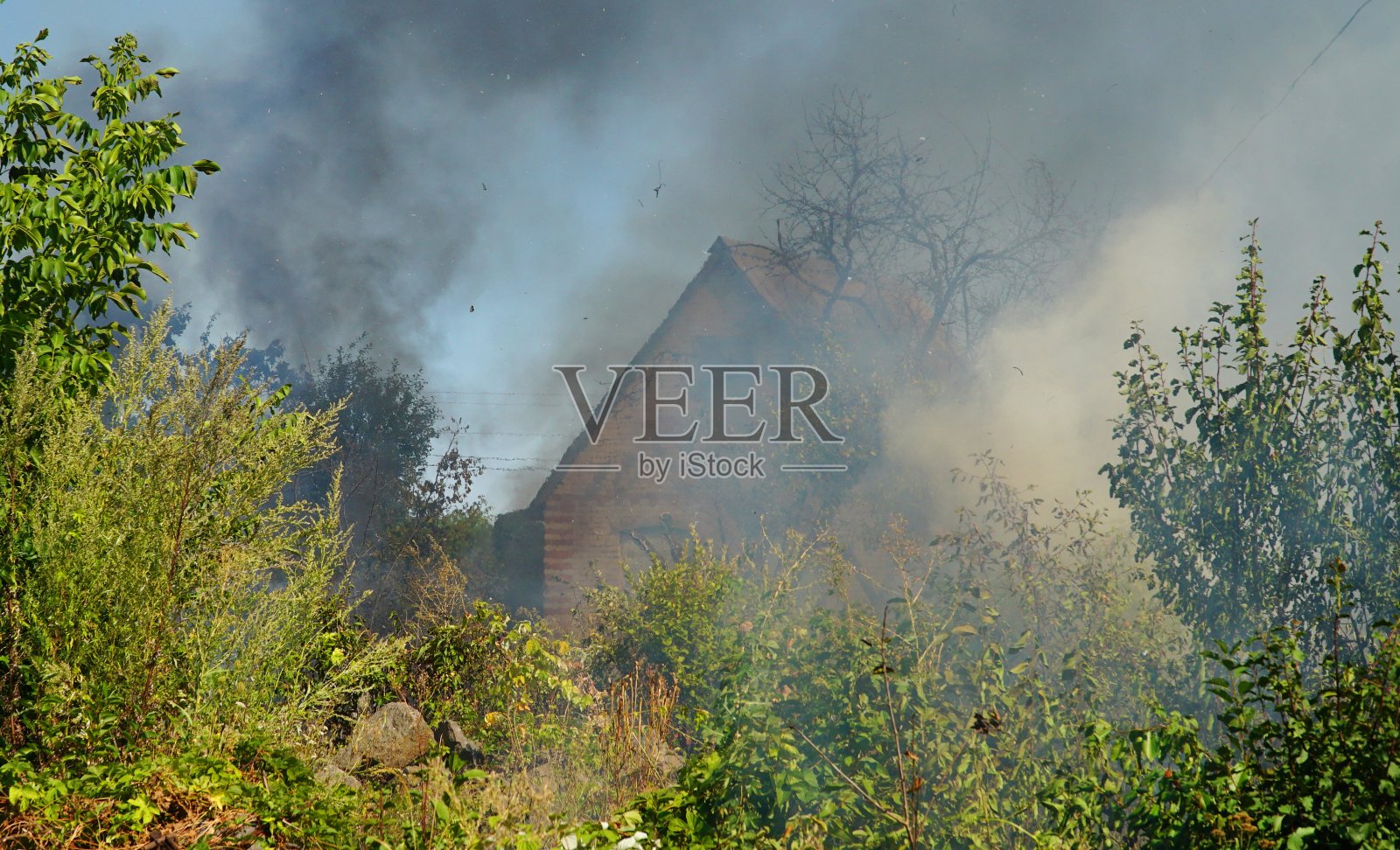 房子着火了。房子被火烧毁了。从着火的房子的屋顶冒出的烟。烧毁房屋的遗迹。照片摄影图片