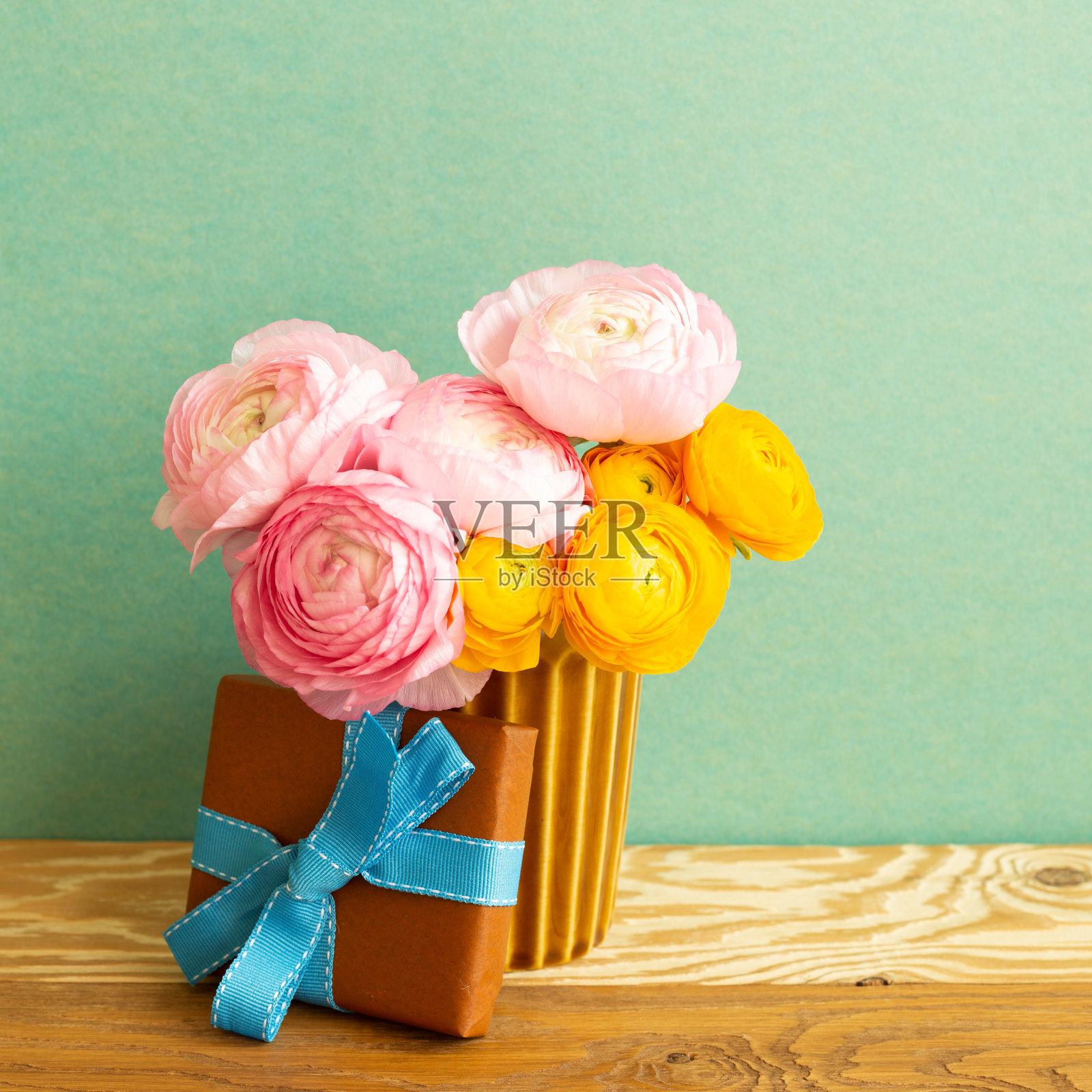 木桌上放着棕色礼盒和毛茛花花束。绿色背景照片摄影图片