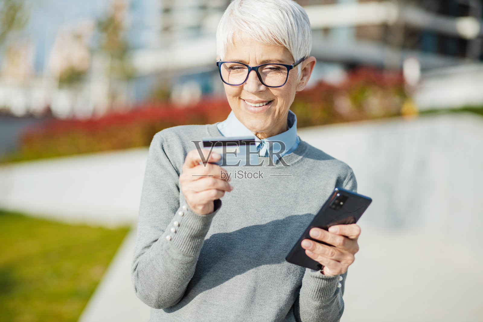 一位资深女士正在用信用卡进行户外网上购物照片摄影图片