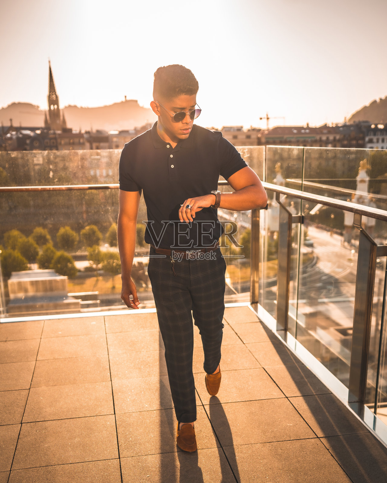 时尚的生活方式，一个年轻的拉丁美洲人的肖像与圣塞巴斯蒂安市的背景，Gipuzkoa。蓝色马球衫和格子裤，在夕阳下漫步照片摄影图片