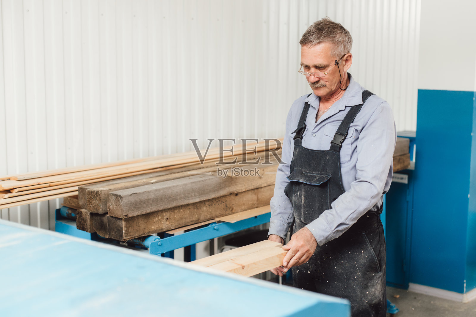 一个年老的木匠或木匠在木匠作坊里用木板工作的肖像照片摄影图片
