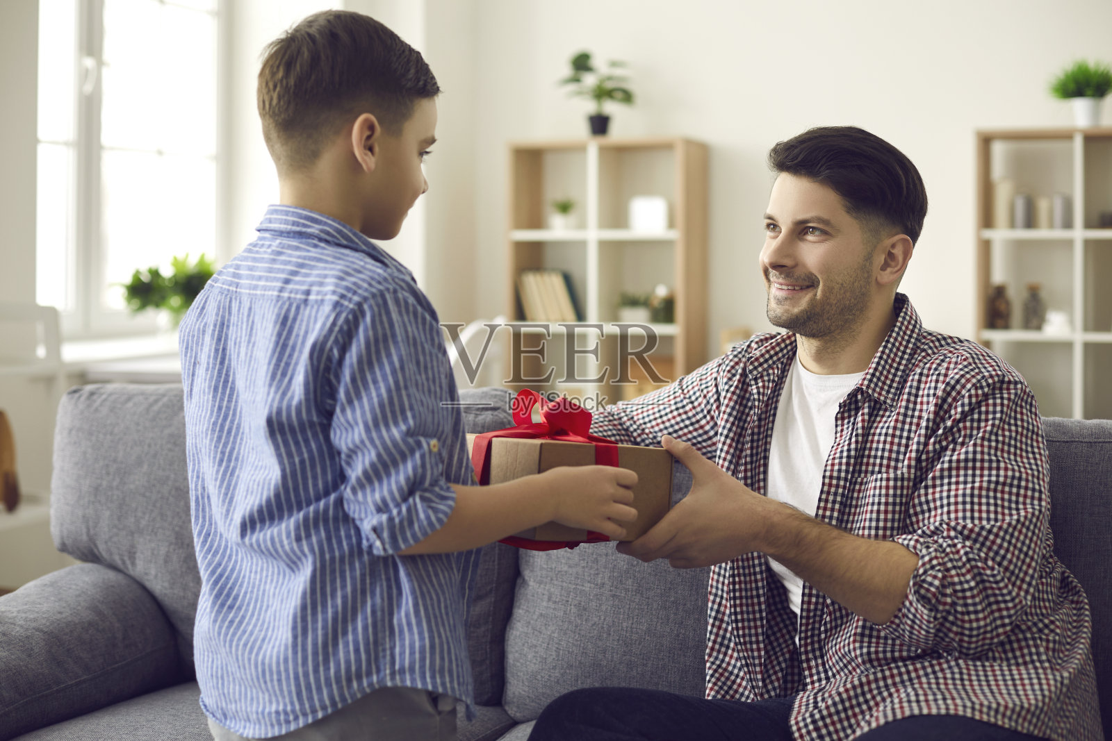 快乐微笑的父亲坐在沙发上，从儿子手中接过惊喜礼盒照片摄影图片