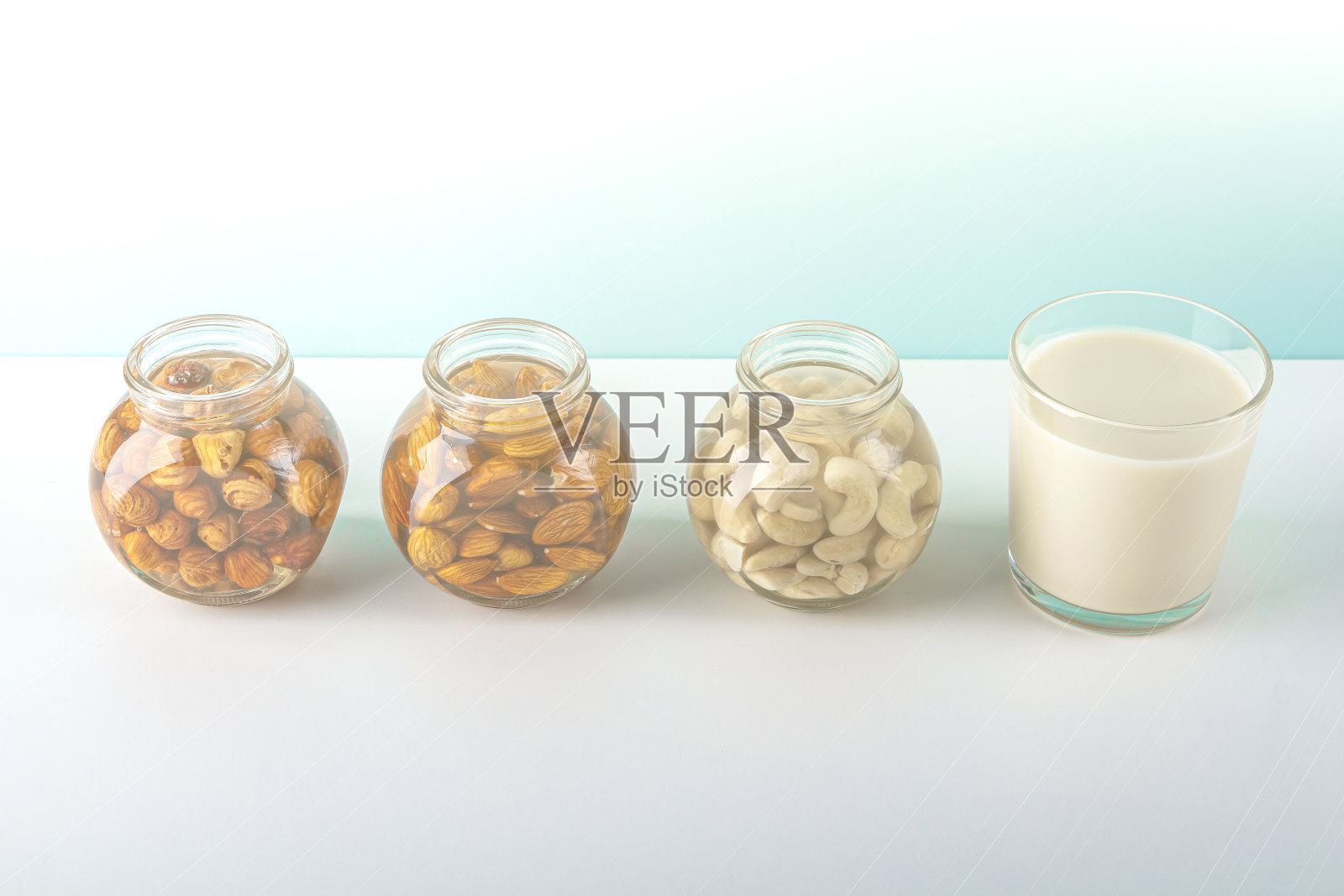 浸泡各种坚果的过程:杏仁、榛子、腰果在水中活化和一杯蔬菜奶。家庭烹饪:以植物为基础的有机蔬菜牛奶，不含乳糖。照片摄影图片