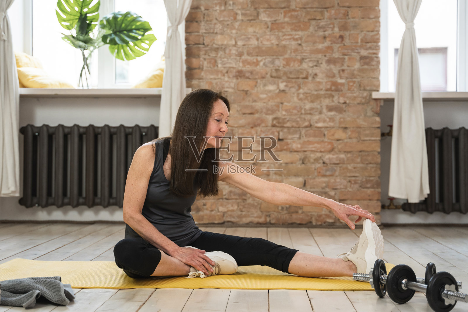 一位老年妇女在家健身时坐在黄色的垫子上伸展身体照片摄影图片