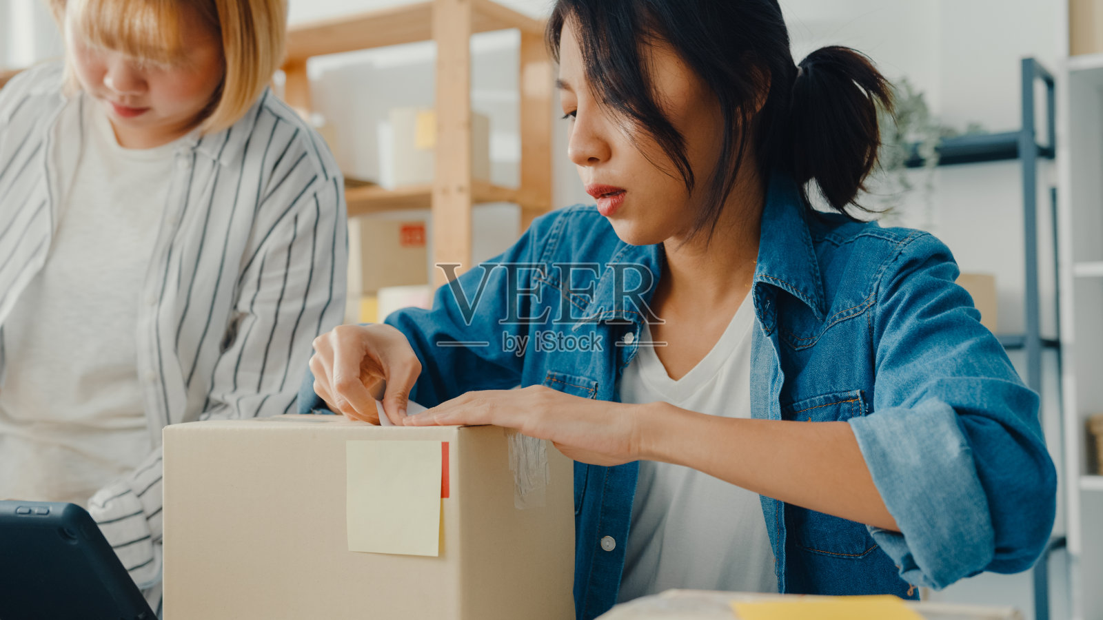 年轻的亚洲商业女性使用移动电话接收采购订单，并在家中办公室检查产品库存。照片摄影图片