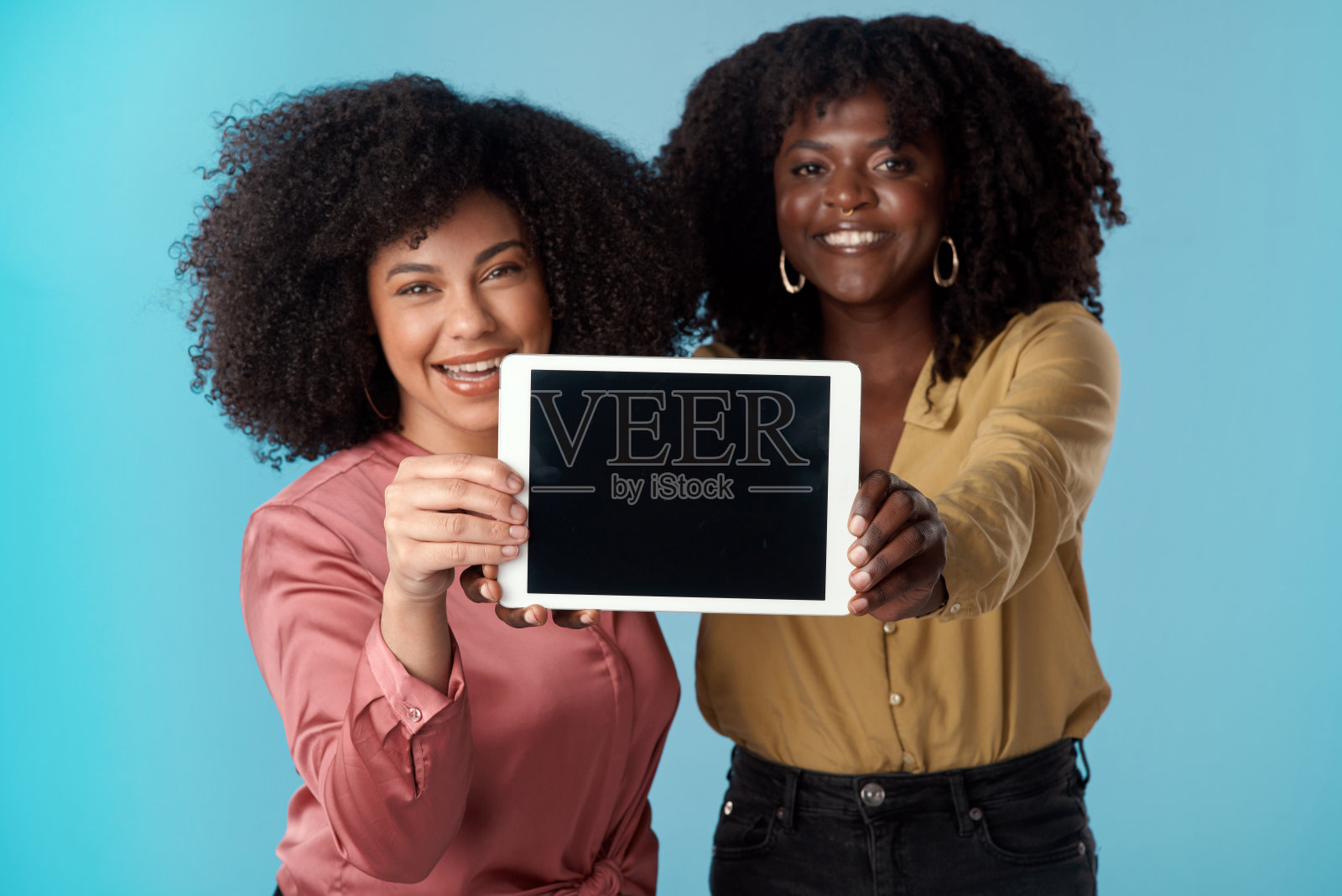 工作室拍摄了两名年轻女性拿着一个蓝色背景下的空白屏幕的数字平板电脑照片摄影图片