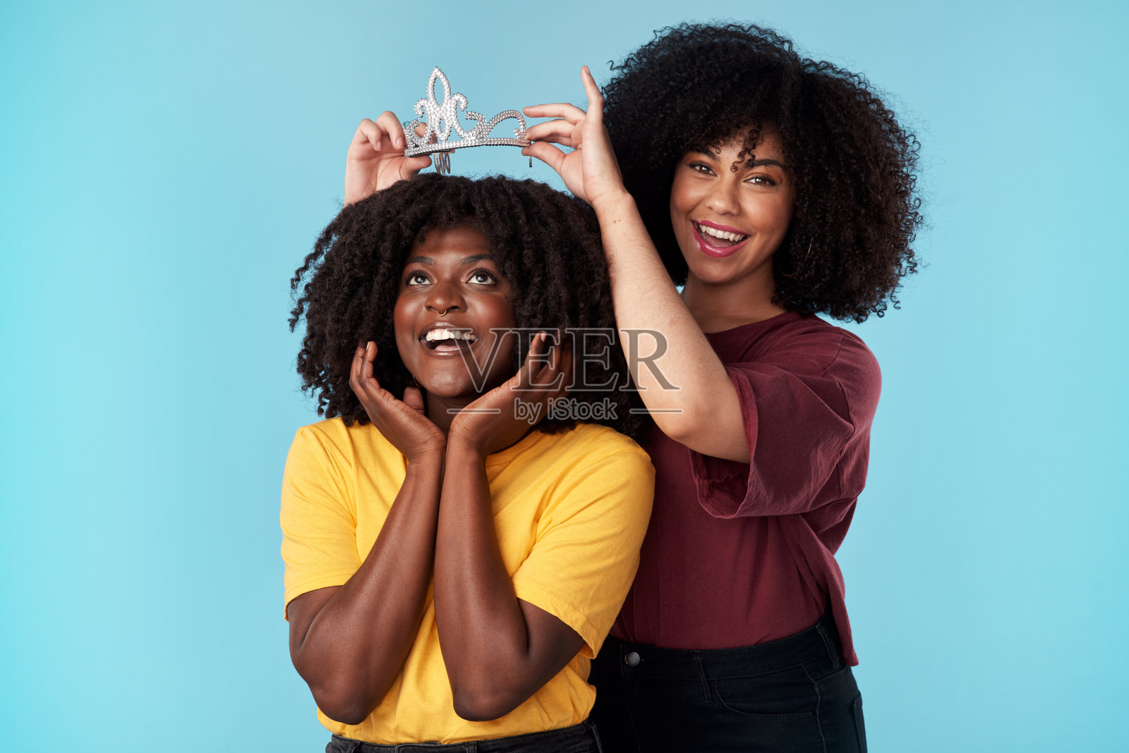 一名年轻女子在蓝色背景下给她的朋友戴上一顶皇冠照片摄影图片