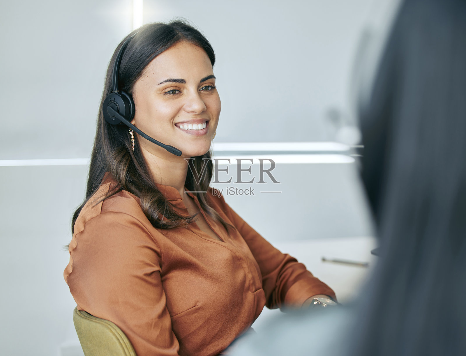 一个漂亮的年轻女销售员戴着耳机和同事坐在办公室里照片摄影图片