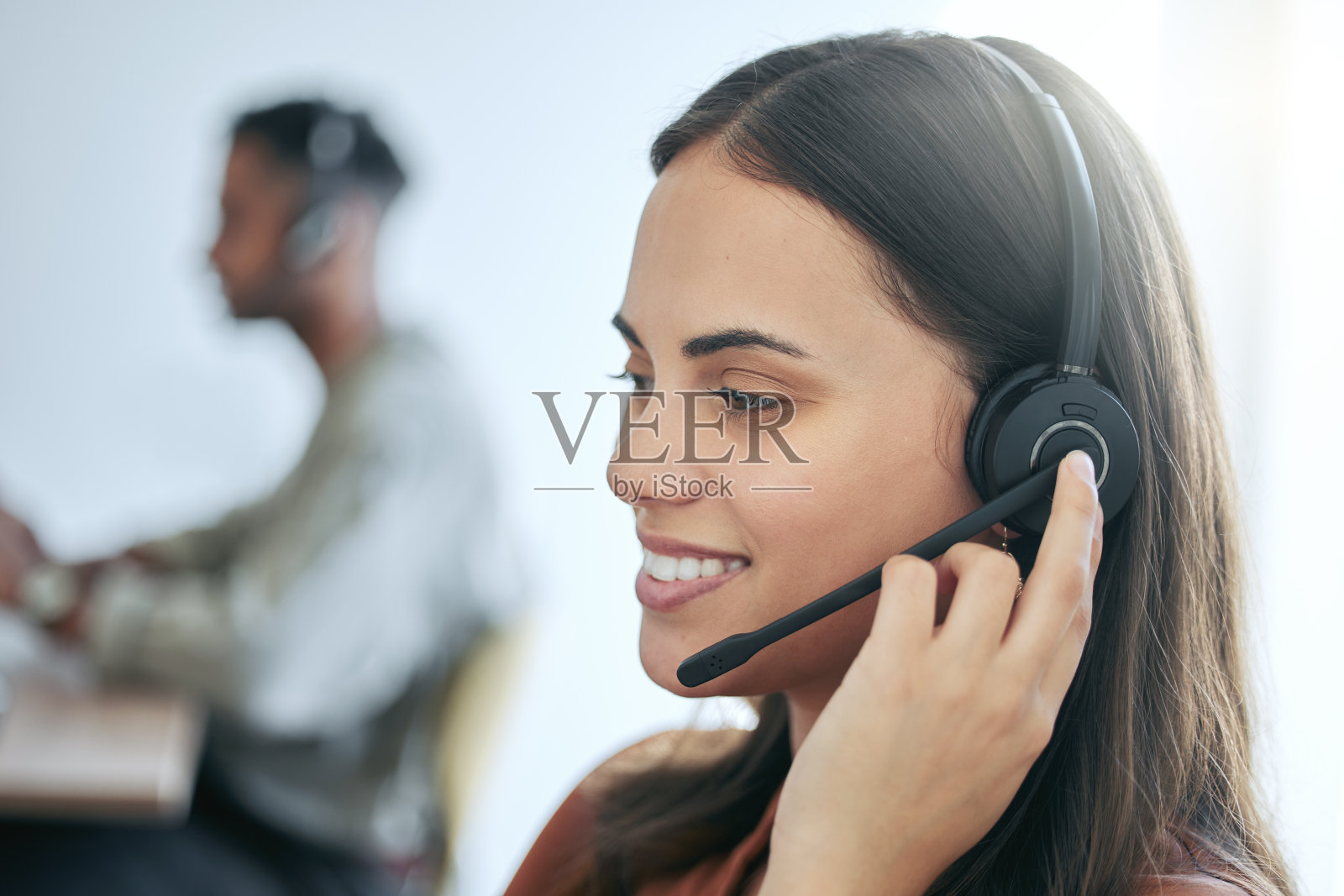 一个漂亮的年轻女销售员戴着耳机和一个同事坐在办公室里照片摄影图片