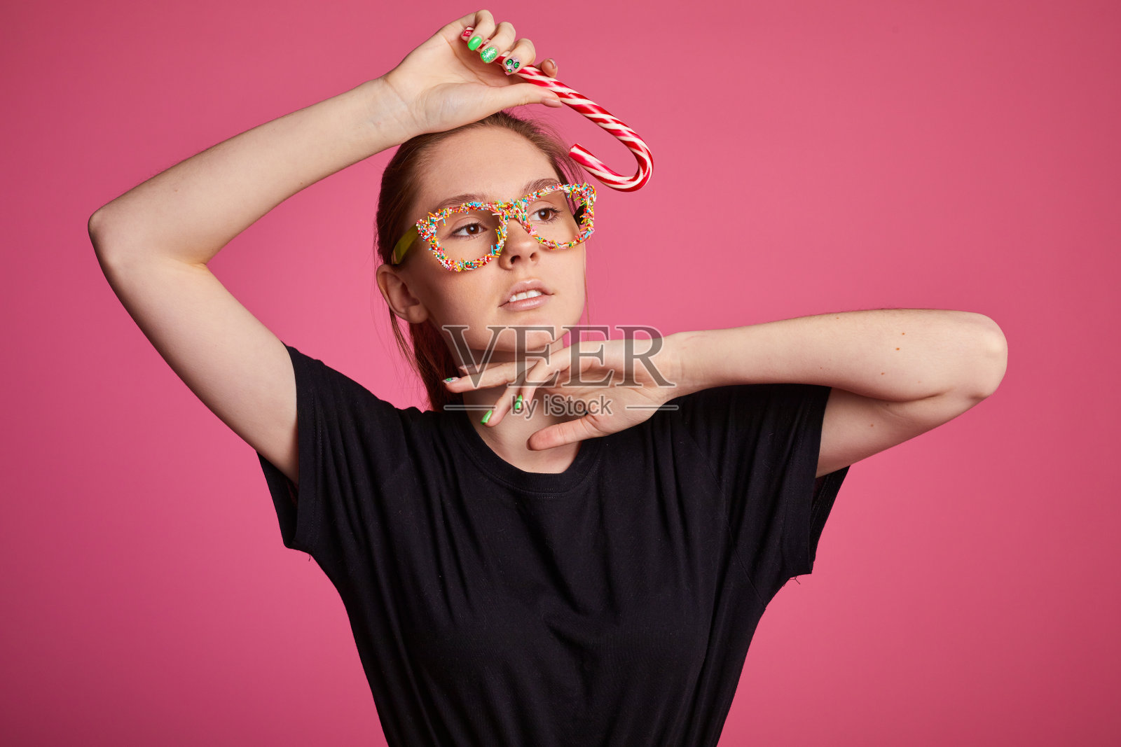 美丽性感的年轻女孩在红色的裙子和甜蜜的洒眼镜拿着一个节日糖果拐杖在红色的背景。照片摄影图片