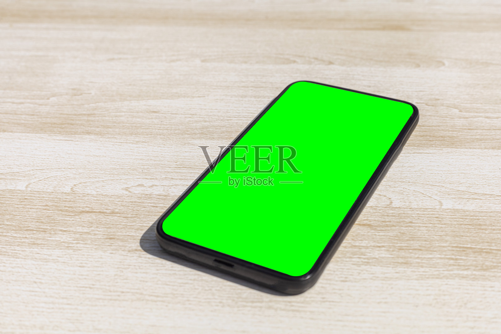 在一个阳光明媚的日子里，黑色的智能手机放在一张浅色的木桌上，屏幕是绿色的照片摄影图片