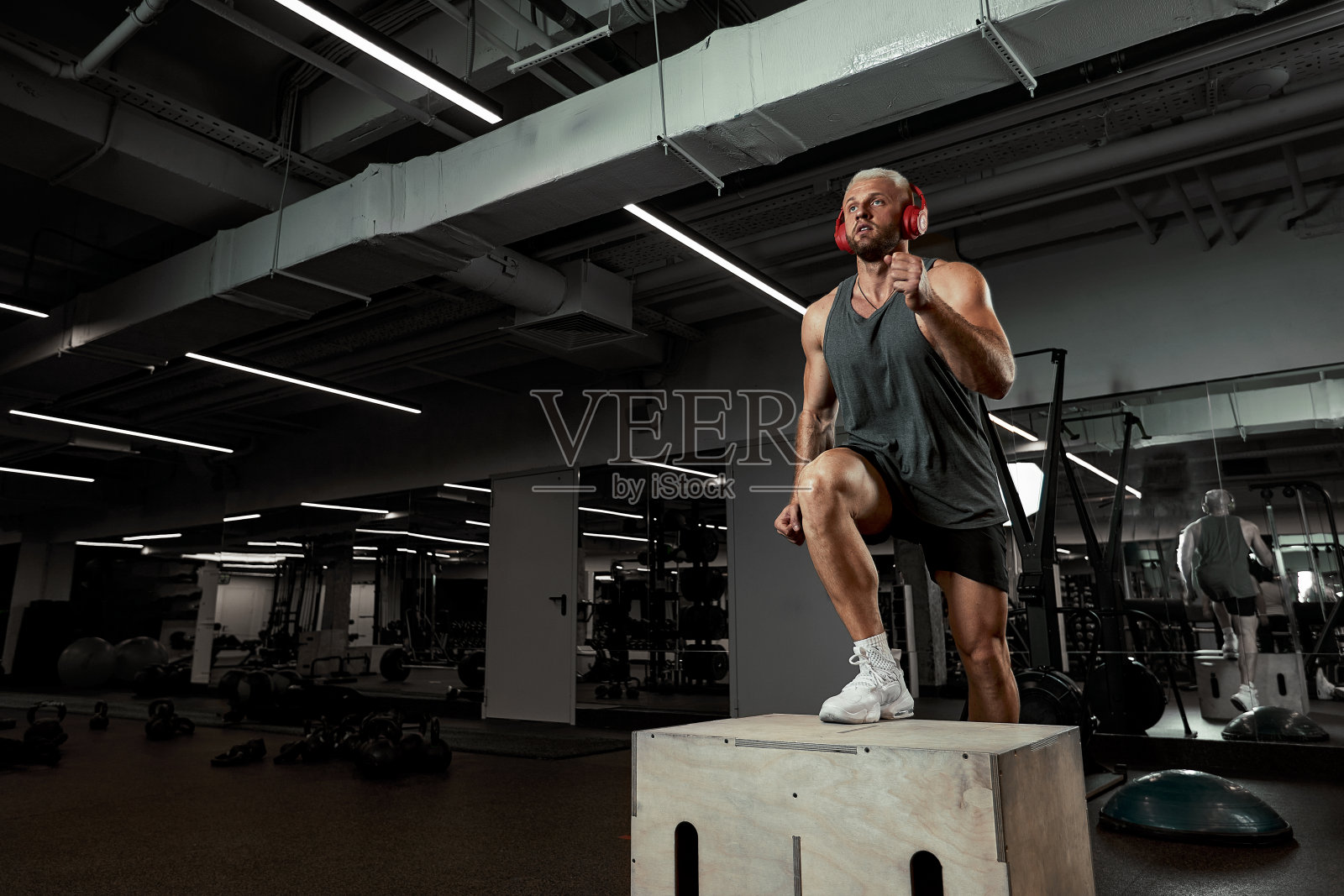 性感的肌肉男使用平台为他的腿在深色的彩色背景的健身房照片摄影图片