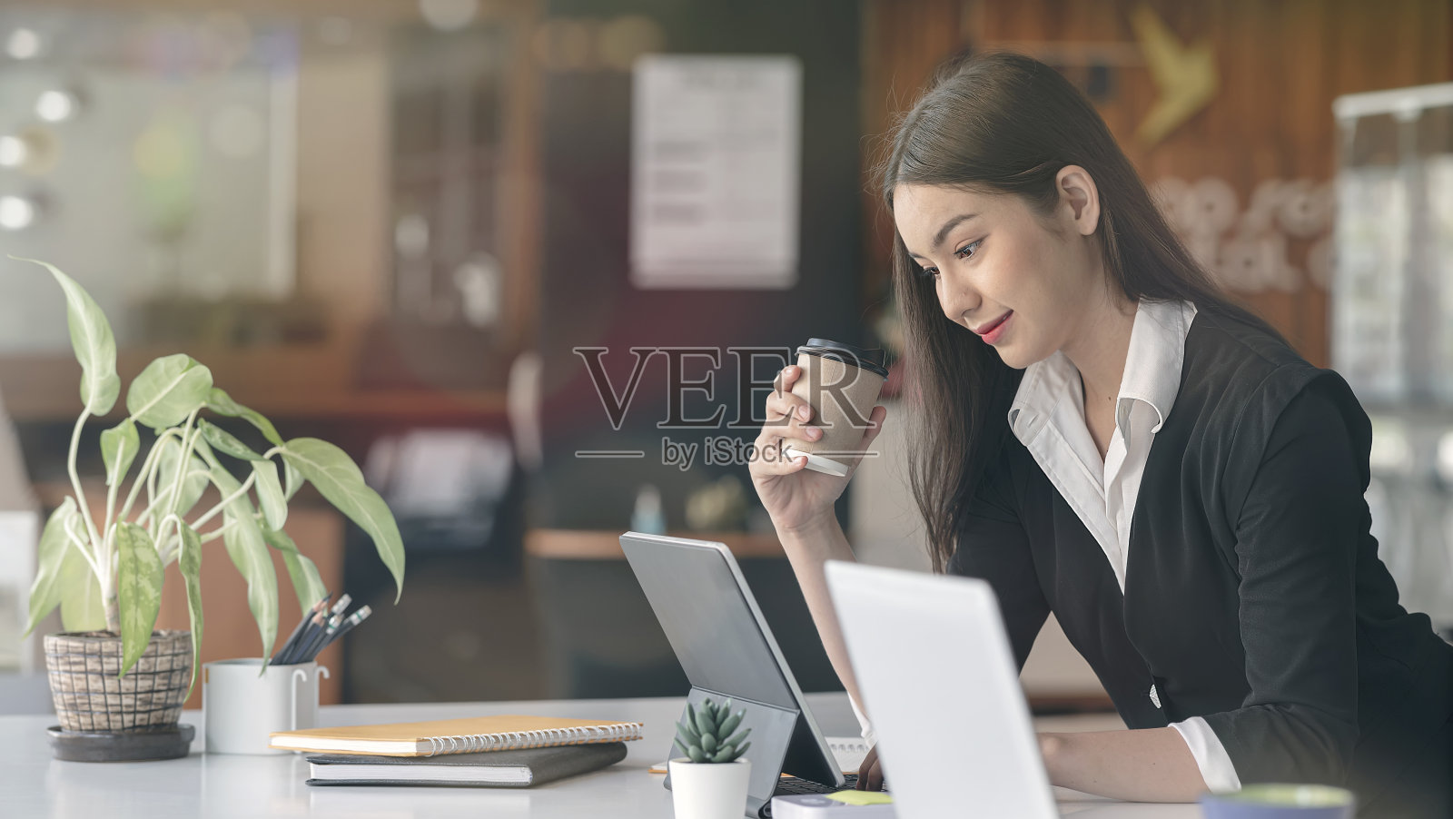 年轻美丽的女商人拿着一杯咖啡，在办公室用笔记本电脑工作。照片摄影图片