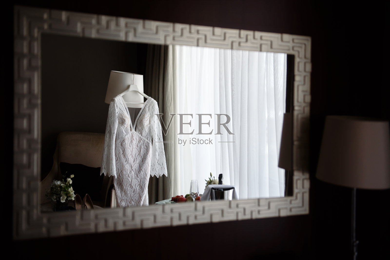 美丽的米色婚纱在酒店房间的镜子里反射，复制空间。新娘的鞋和耳环站在沙发上照片摄影图片