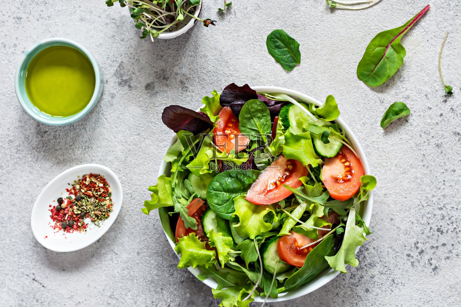 在灰色背景的碗里放上新鲜蔬菜，成熟的西红柿，黄瓜，生菜和微绿色蔬菜。健康生食理念。照片摄影图片