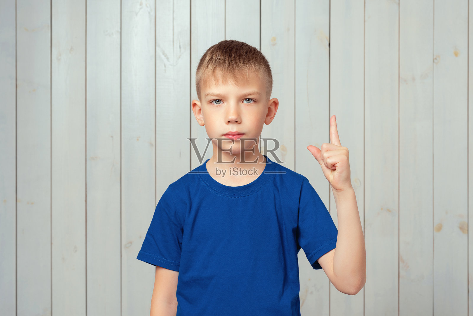一幅穿着蓝色t恤的严肃的十几岁男孩的画像，用手指向上给人建议，说:请注意照片摄影图片