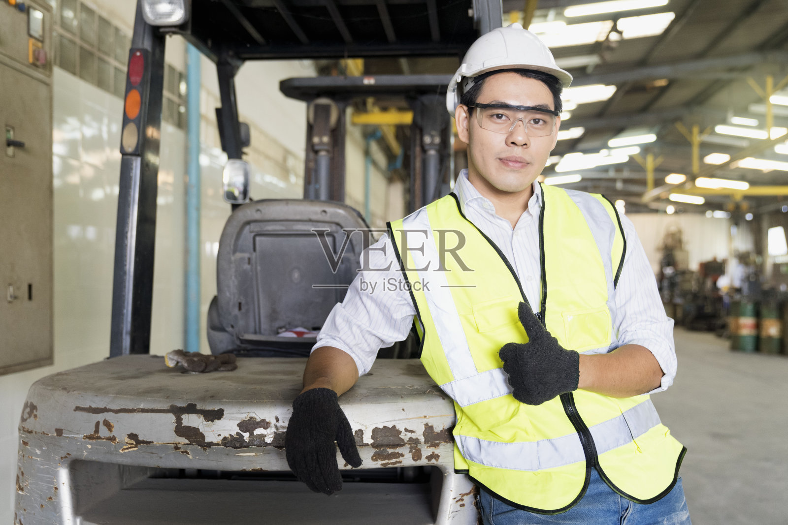 技术员竖起大拇指。工头或技术员站在工厂的叉车旁边。照片摄影图片