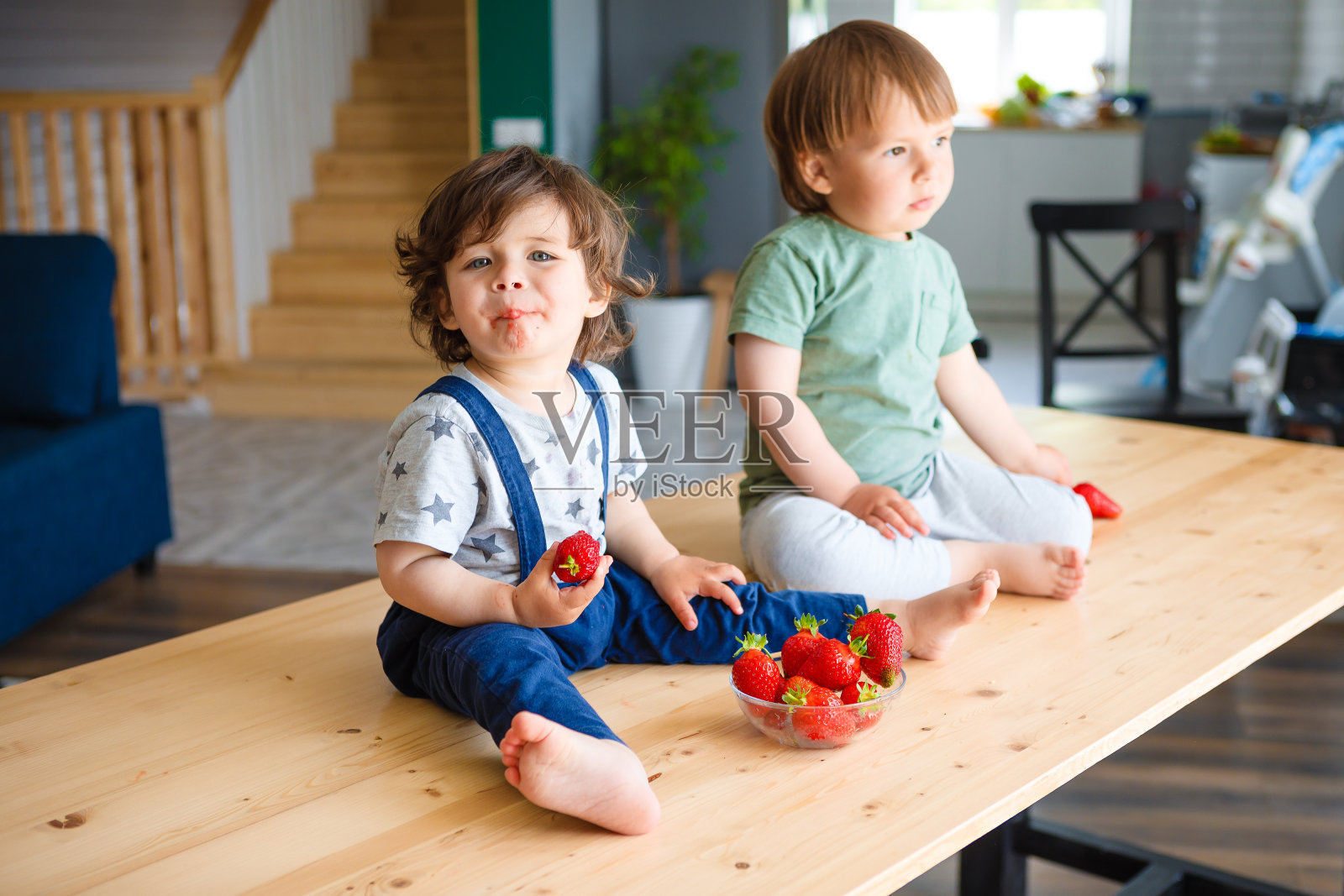 小弟弟们正坐在厨房的木桌上吃草莓。照片摄影图片