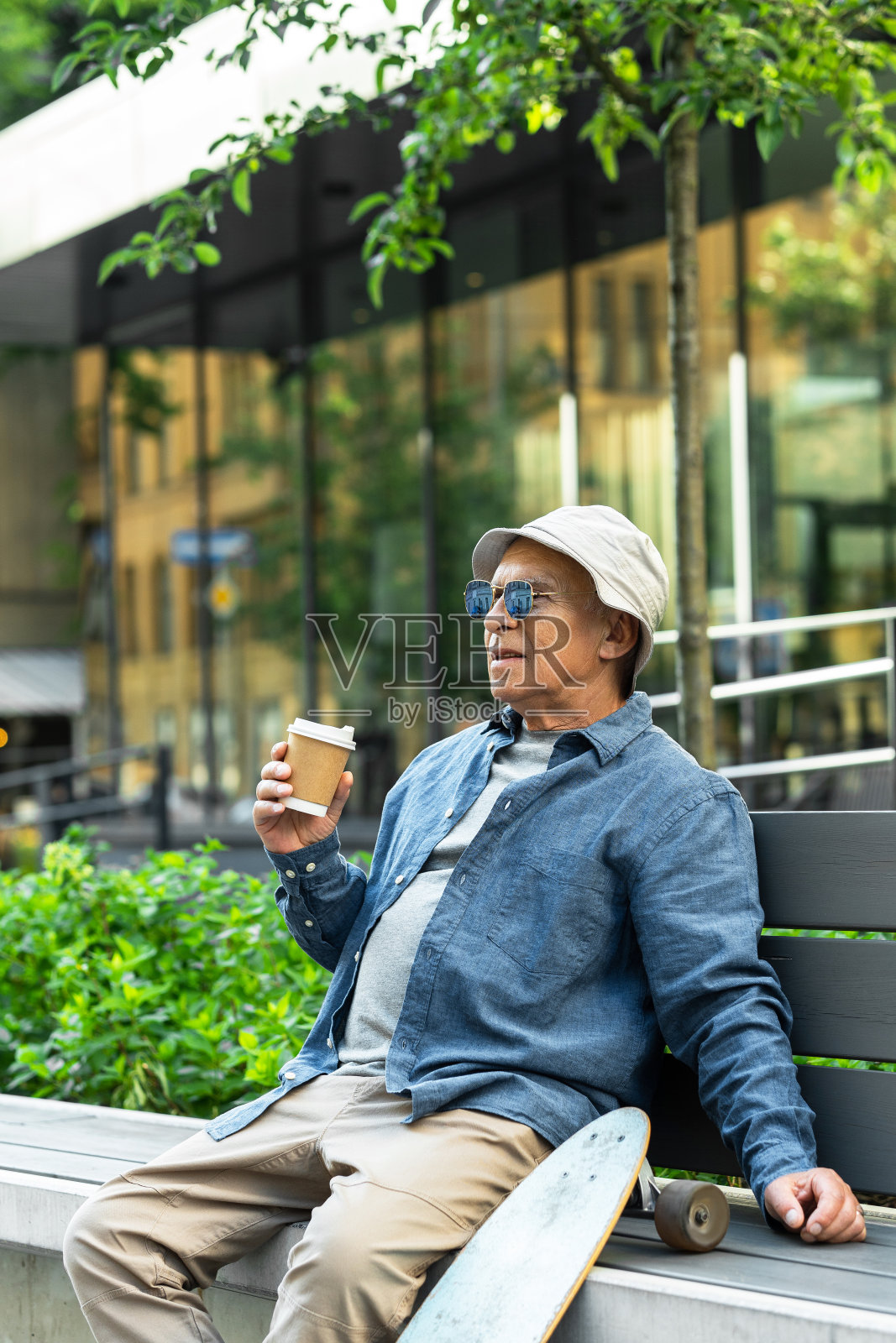 一个老人带着长板坐在城市公园的长椅上喝咖啡照片摄影图片