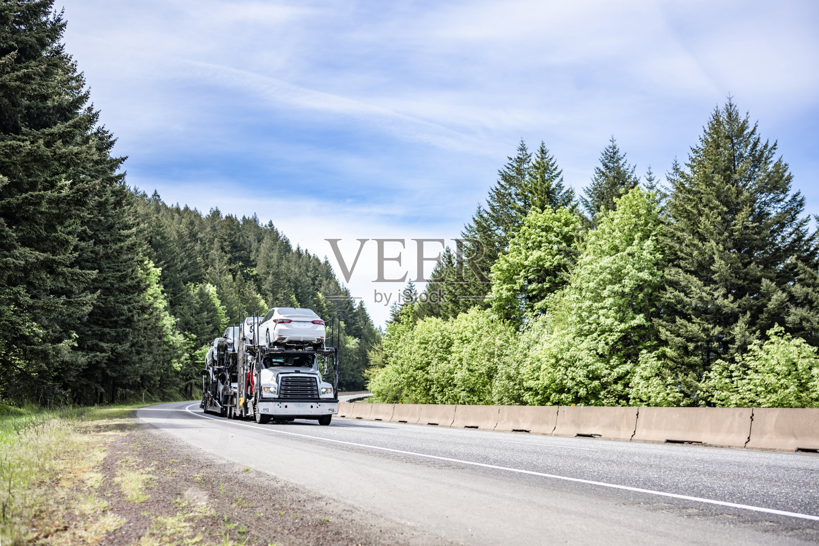 紧凑的日驾驶室，大型钻机，白色汽车拖车，半挂车运输汽车上的两层半挂车运行在蜿蜒的森林道路上照片摄影图片