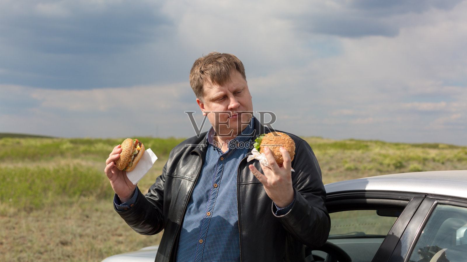 在新鲜空气中，一名饥饿的男子在两个汉堡中做出选择照片摄影图片