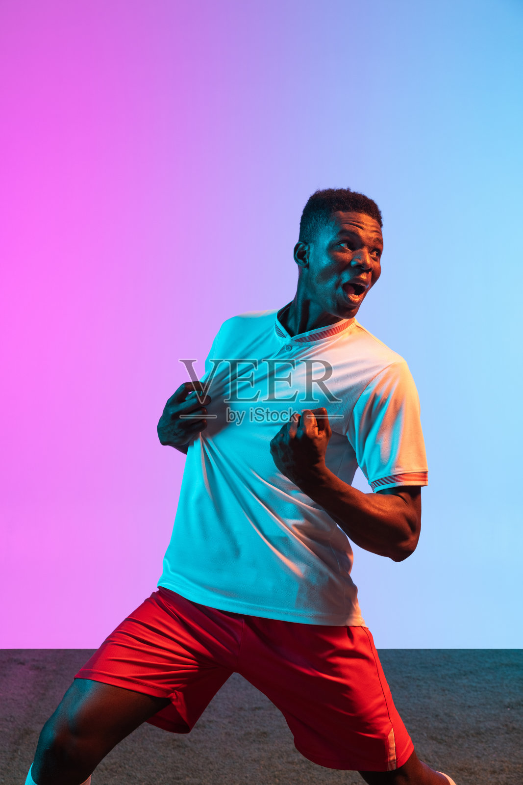 特写非洲人，职业足球运动员孤立地站在渐变蓝粉色背景霓虹灯。照片摄影图片