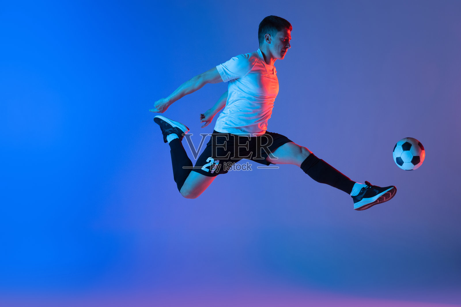 年轻的白人男子，男性足球运动员跳孤立在梯度蓝粉色背景霓虹灯照片摄影图片