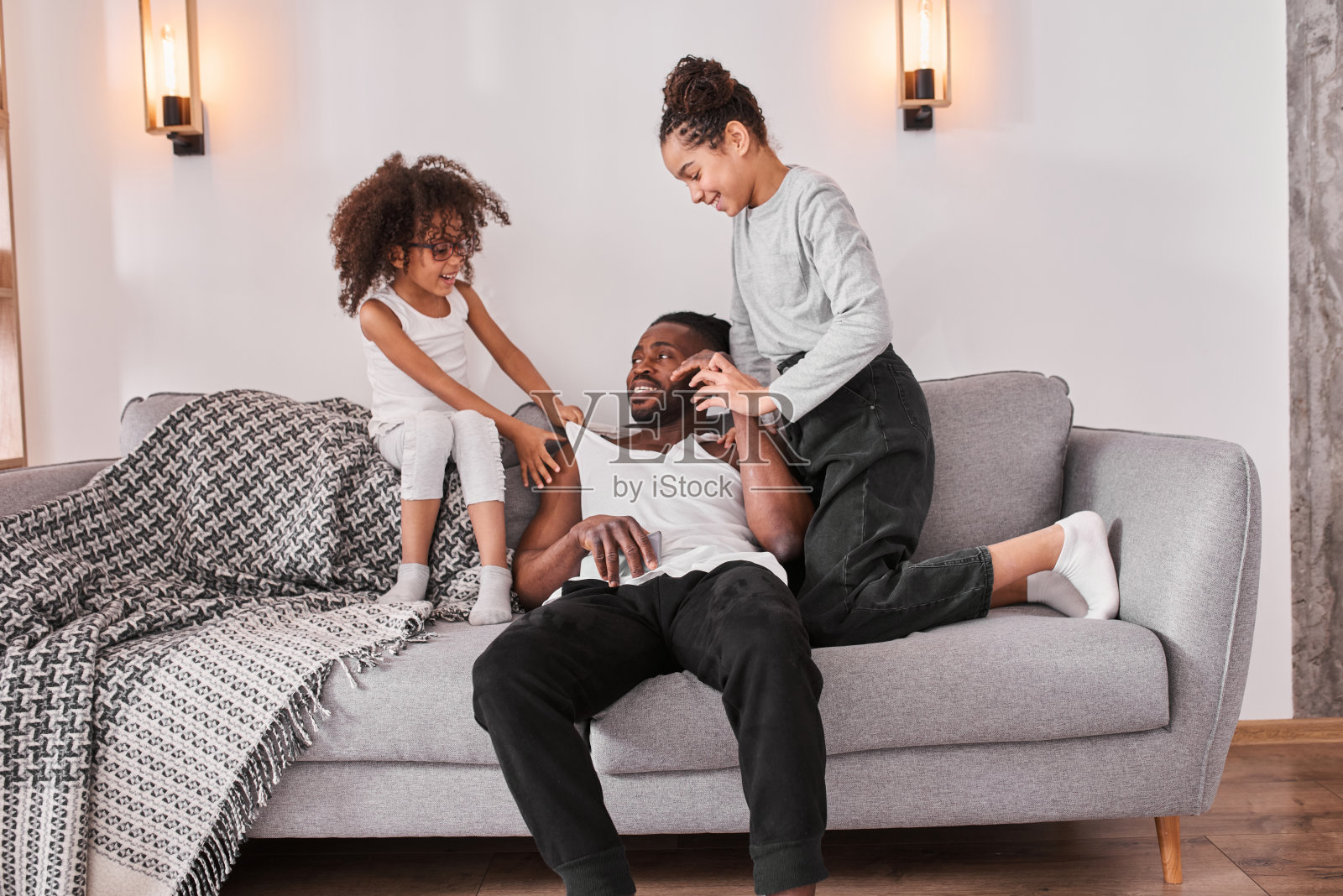 父亲坐在沙发上休息，而他的有趣活泼的女儿们在玩耍照片摄影图片