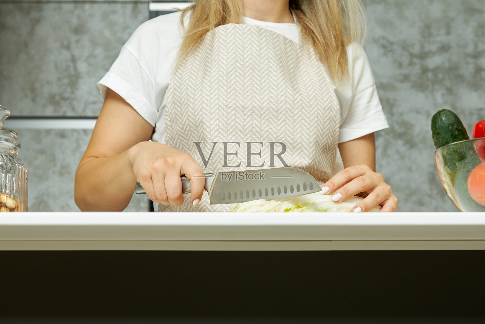 厨房里的女人拿着刀切菜。照片摄影图片