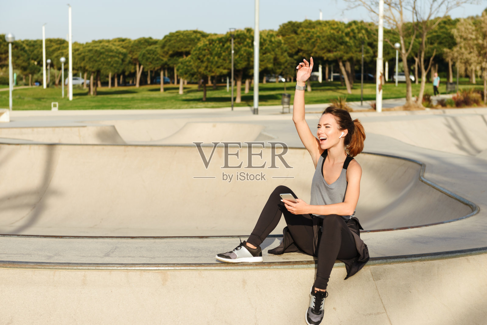 体育女士坐在户外公园向朋友挥手。照片摄影图片