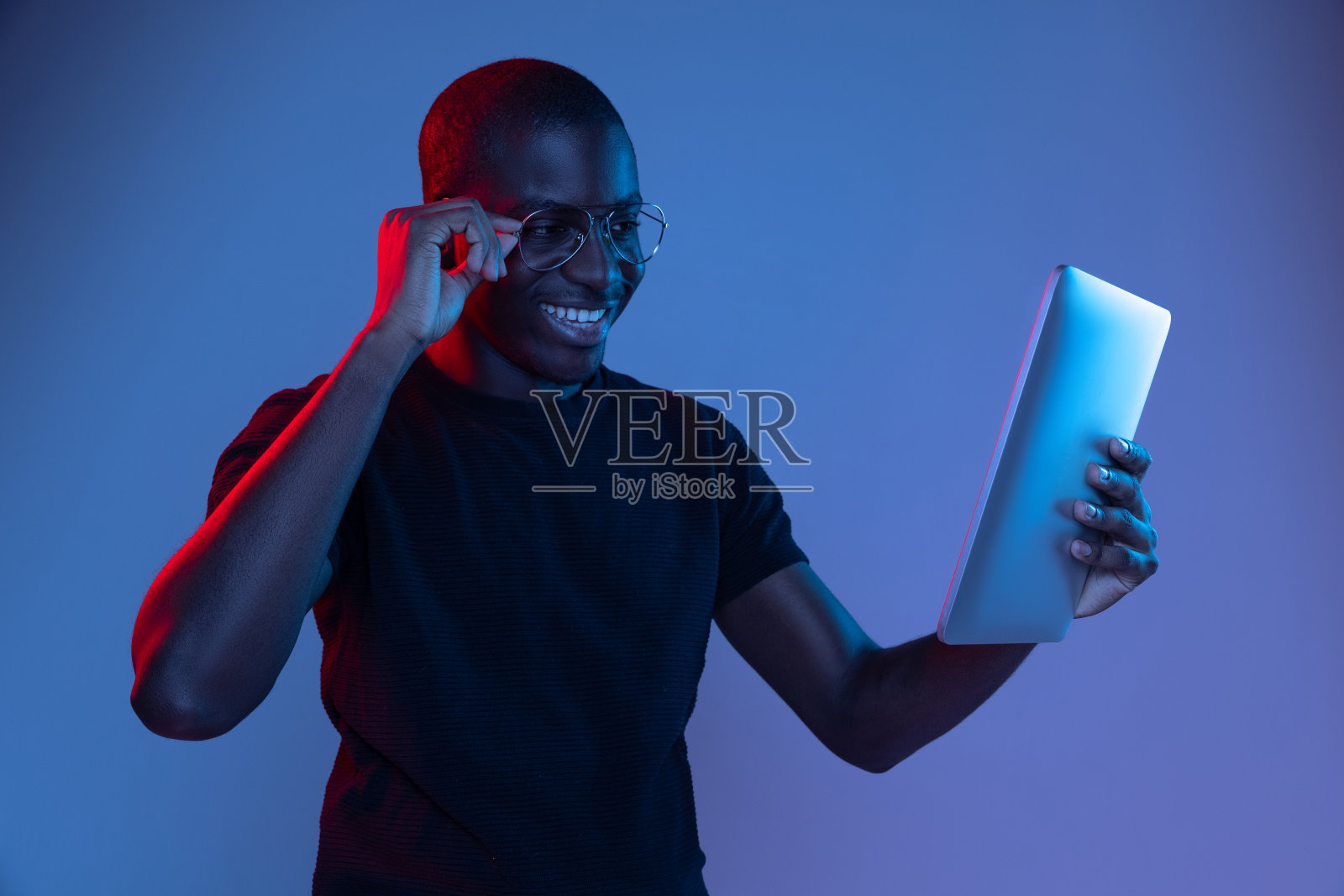 快乐年轻的非洲英俊男子与平板电脑隔离在黑暗背景在混合霓虹灯。照片摄影图片