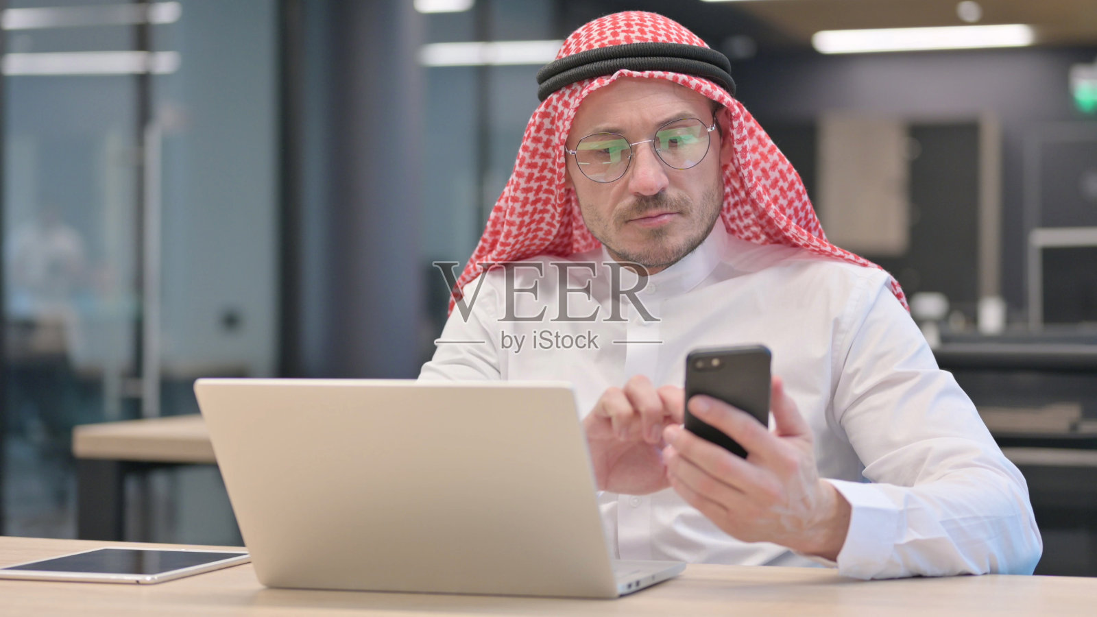 在办公室里，中年男人用笔记本电脑使用智能手机照片摄影图片