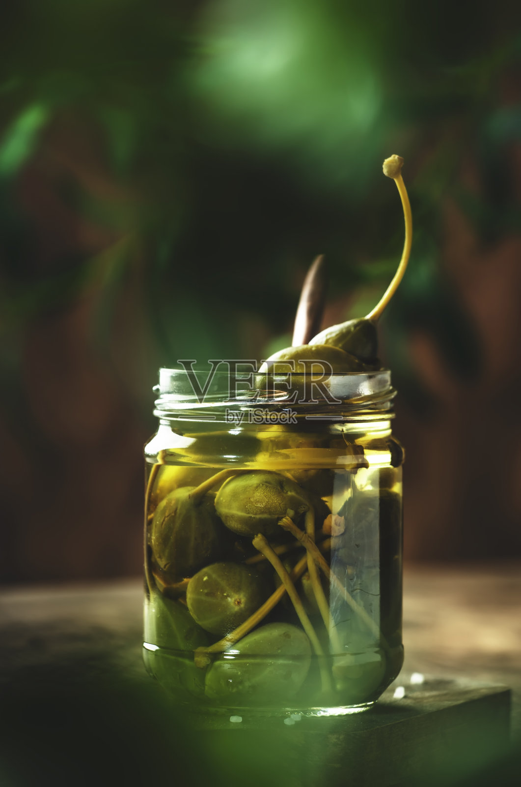 酸豆。腌制的山柑果罐头放在玻璃罐中，放在木桌上，生态风格的静物照片摄影图片