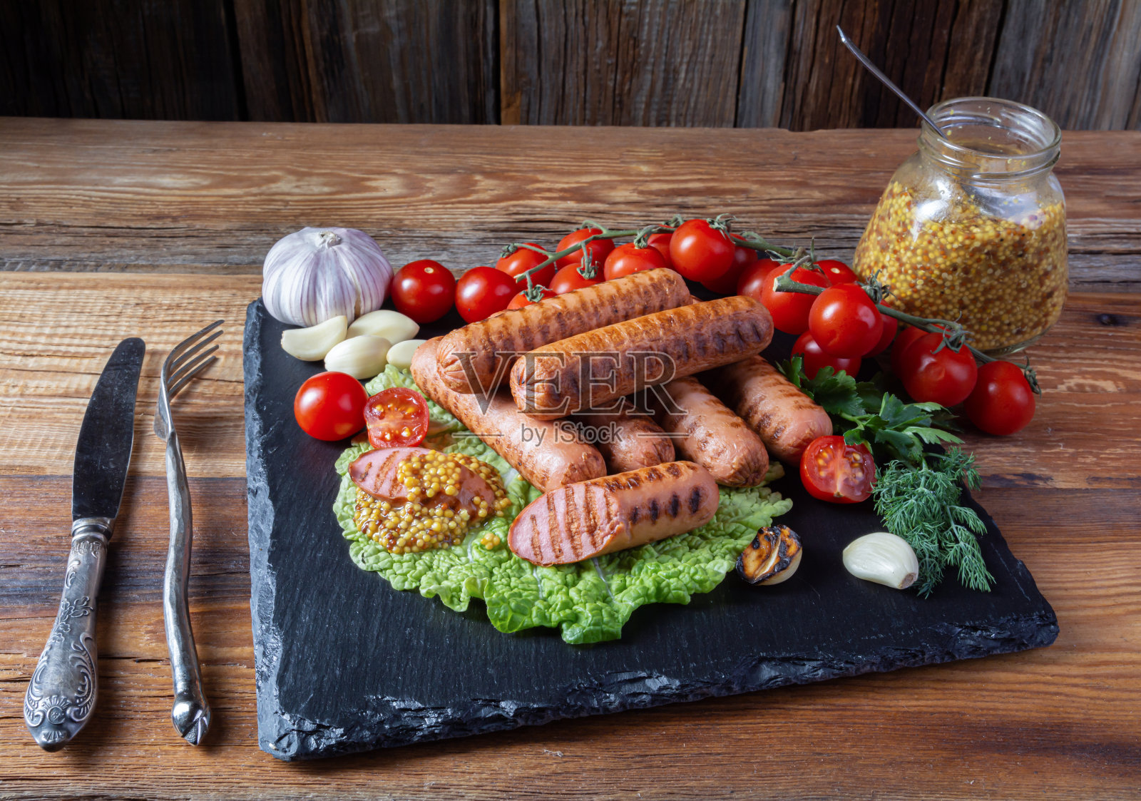 烤香肠，圣女果，大蒜，莳萝，一罐芥末，刀，叉放在木桌上，俯视图照片摄影图片