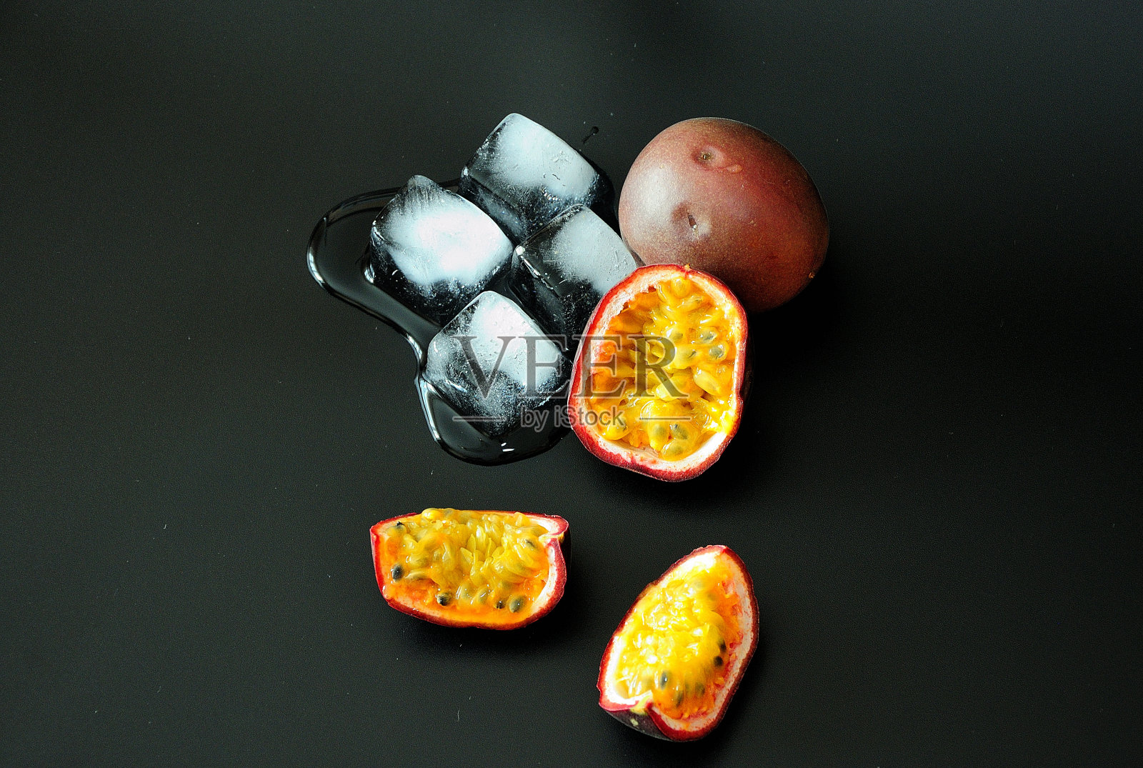熟透的西番莲果切成块和融化的冰块在黑色的背景。照片摄影图片