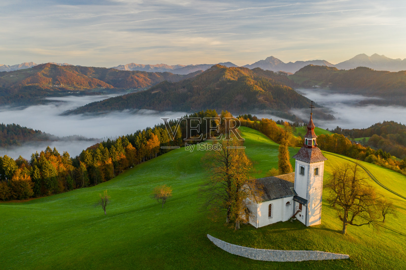 鸟瞰图的山，彩色森林在雾和教堂Sv Tomaz。斯洛文尼亚秋天的日出照片摄影图片