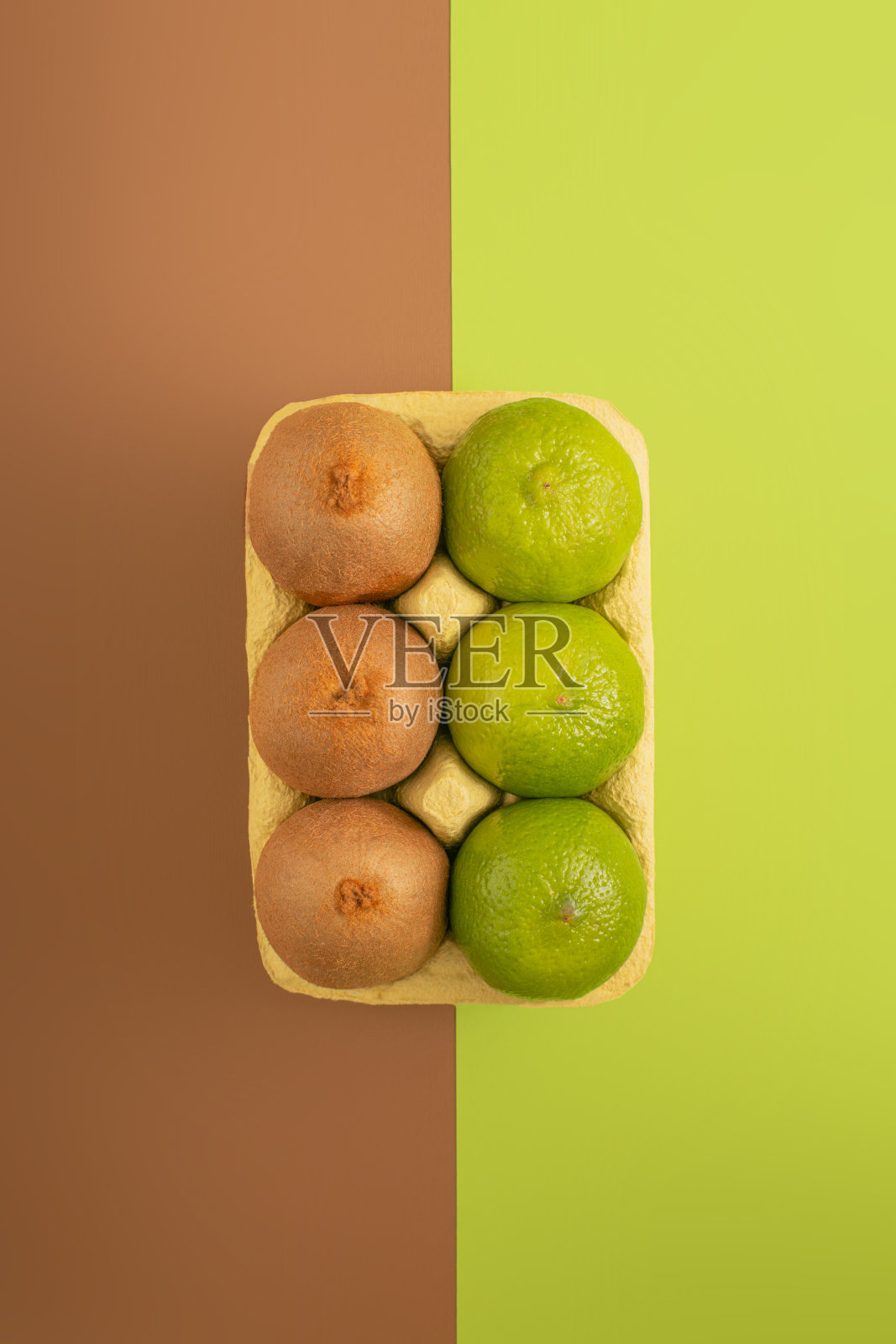 极简的热带水果理念与新鲜的有机猕猴桃和酸橙在鸡蛋包装明亮的绿色和棕色的背景。简单的垂直平铺构图，创意素食健康食品理念。照片摄影图片