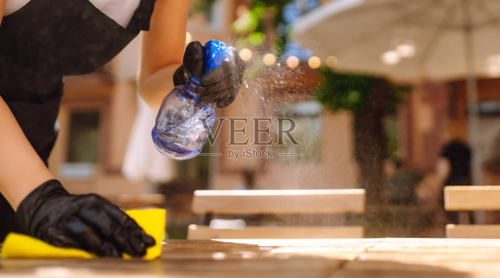 清洁消毒餐桌，预防COVID-19。近距离拍摄在冠状病毒疫情期间用消毒剂清洁餐桌的服务员。照片摄影图片