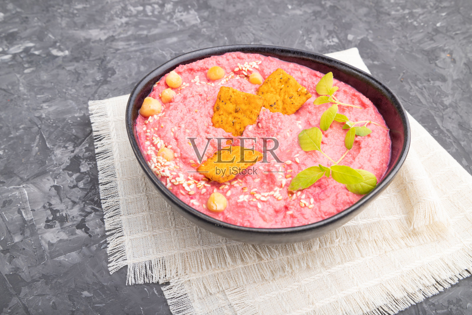 鹰嘴豆泥、甜菜和微绿色罗勒芽放在陶瓷碗里，黑色混凝土背景和亚麻织物。侧视图，特写。照片摄影图片