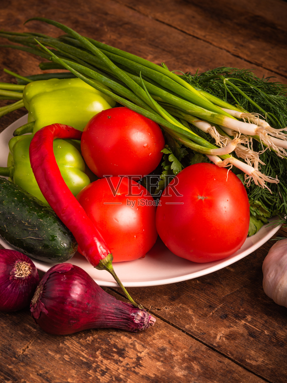 一套蔬菜作为一天的素食餐。新鲜的蔬菜放在一个盘子里，背景是乡村的木头，洋葱，西红柿，黄瓜，辣椒，大蒜照片摄影图片