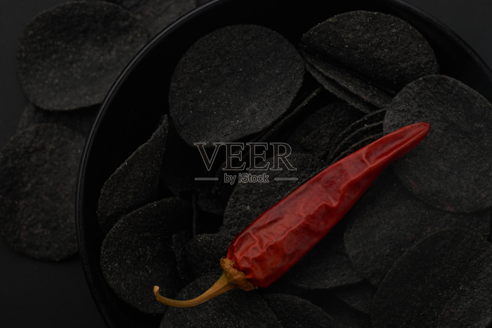 黑色背景下的黑薯片和红辣椒照片摄影图片