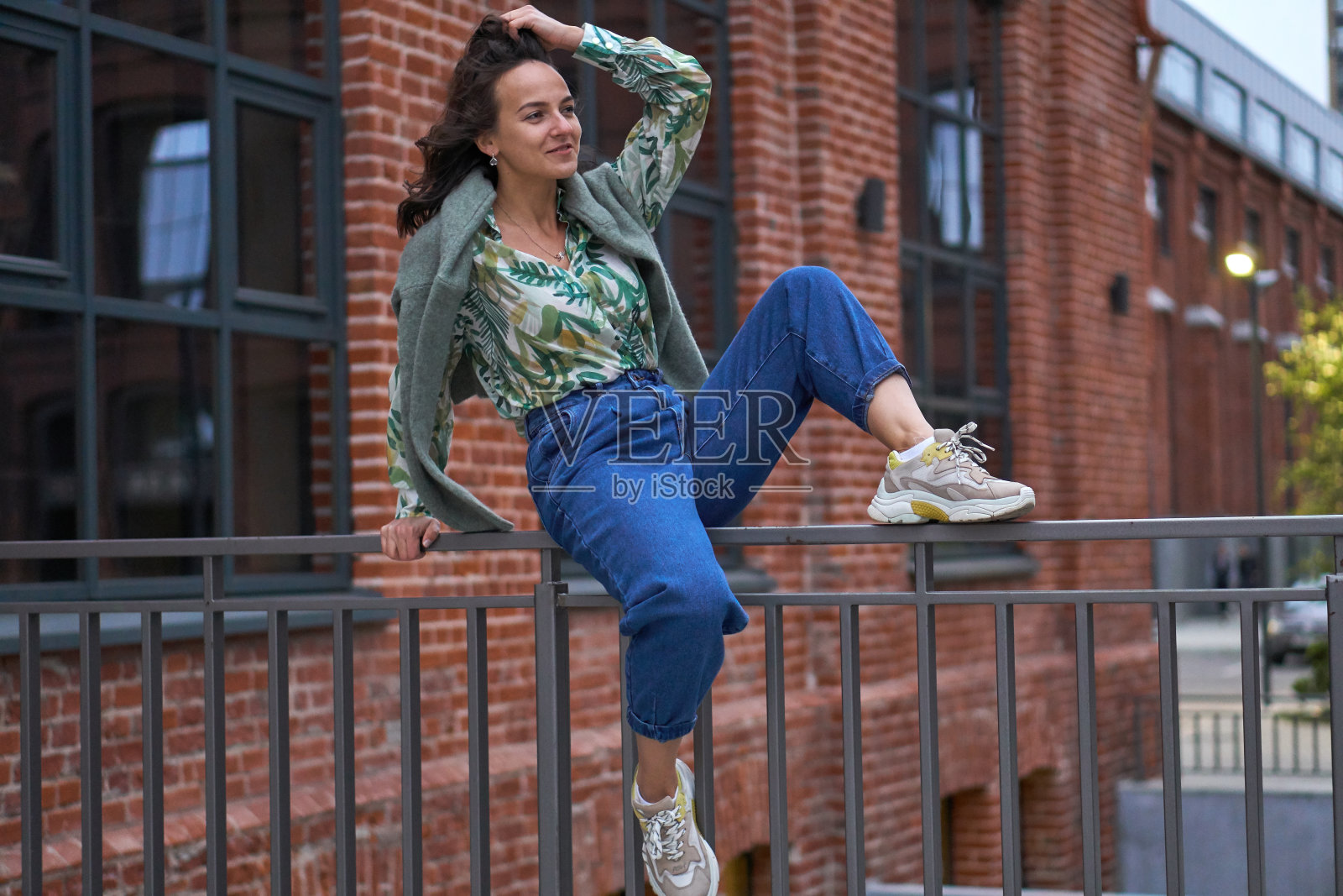 一个穿着牛仔裤的年轻女子坐在栏杆上。校园。照片摄影图片