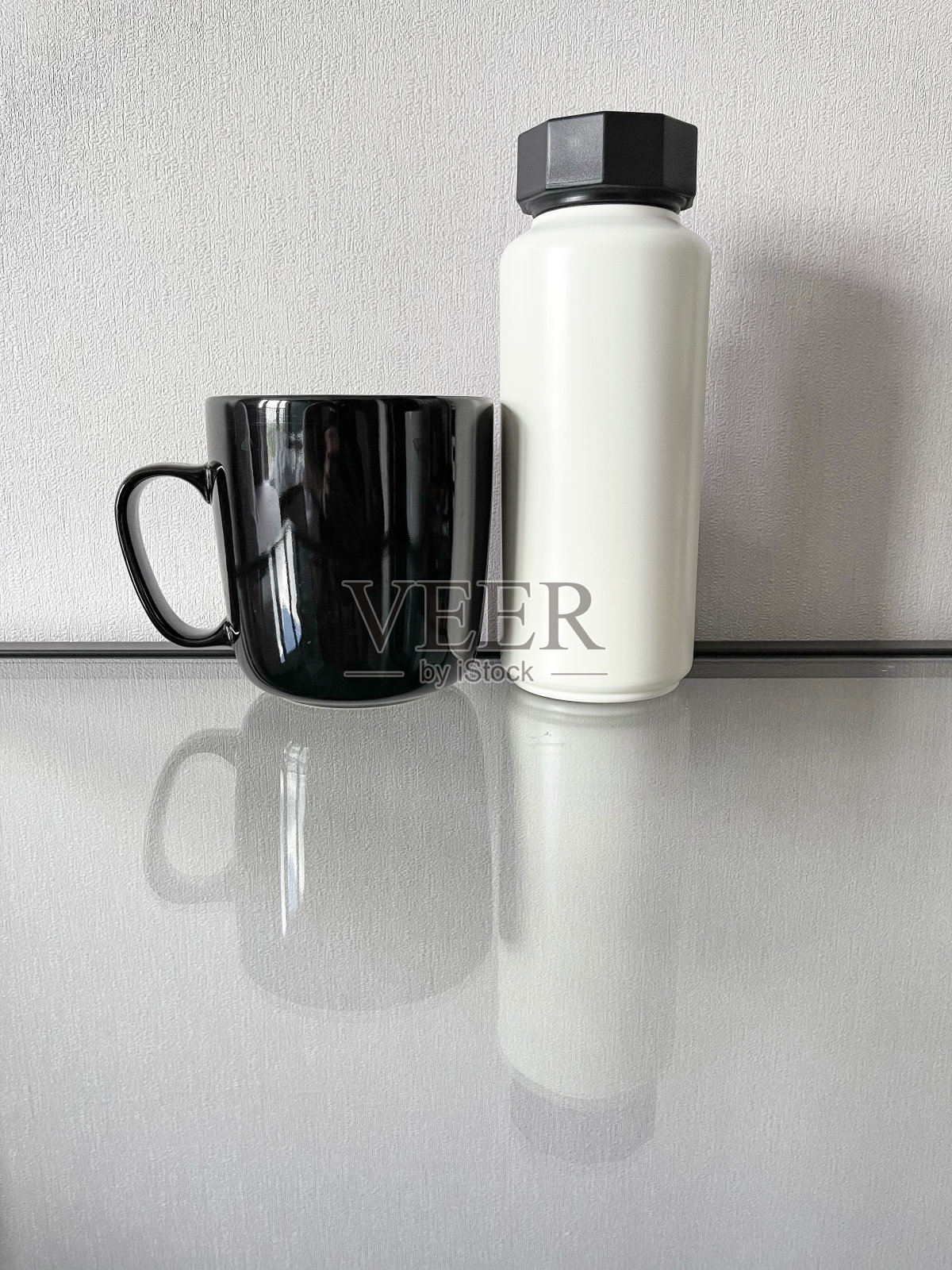 玻璃桌上有一只黑色的杯子和一个白色的瓶子照片摄影图片